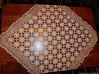Full view of the crocheted tablecloth displaying the diamond shape with intricate circular flower pattern and delicate crocheted edges on a wooden surface.