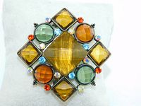Front view of the vintage brooch showing the large central tiger eye like glass stone surrounded by smaller colored stones set in bronze metal.