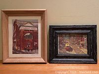 Wide shot showing both framed prints side by side on a beige wall or surface.