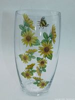 Front view of clear glass vase decorated with yellow daisies and a honey bee transfer on a plain background.