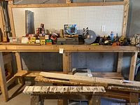 Wooden workbench with assorted tools and hardware on two shelves plus used wooden work surfaces and a stool below
