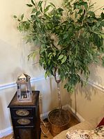 Overall view of the faux ficus tree next to the small wood cabinet and lantern candle holder on top