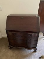 Closed view of antique drop front desk showing dark wood finish, curved drawer fronts and claw feet.