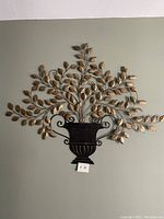 Photo of large metal wall art on wall showing urn and spreading branches with golden leaves.