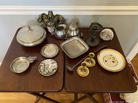 Overview of all pewter and brass items arranged on two wooden tables, showing covered dish, small trays, candlesticks, decorative plate, and other pieces