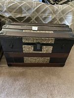 Photo of closed steamer trunk with visible stamped silver inlay, metal corner protectors, and locking mechanism on front.