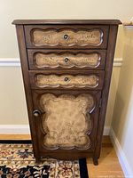 Front view of cabinet showing three drawers and decorative door panel