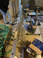 Photo shows the full length of an aluminum Werner Craftmaster extension ladder laid on the floor in a basement or storage area along with other items such as a coiled garden hose, a stationary exercise bike, and a cardboard box with miscellaneous contents.