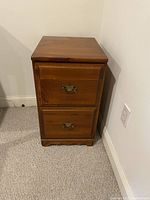 Photo showing the full wood file cabinet with two closed drawers positioned against a wall on carpet.