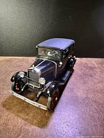 Front angle view of 1/18 scale black diecast 1931 Ford Model A model car by Motor City Models, showing hood, grille, headlights, front bumper, and blue-purple roof.