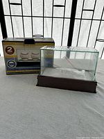 Photo of the dual glass baseball display case alongside its original packaging box showing product details and branding.