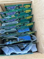 Top-down view showing multiple Brett Favre Starting Lineup figures in original sealed packaging inside a cardboard box, with green and yellow packaging visible.