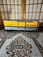 Side view of the G scale Rio Grande box car showing yellow and gray paint with D&RGW and Rio Grande markings.
