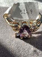 Close-up of ring head showing central purple amethyst and clear accent stone with visible size tag.