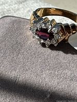 Close-up image of gold tone ring with red and white stones showing detail of setting and stones in sunlight.