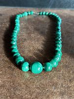 Close-up image of necklace showing large central malachite bead and smaller beads on either side.