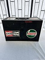 Closed black metal vintage toolbox with Champion and Castrol stickers on front