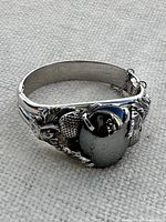 Front and angled side view of the silver tone bracelet showing large black oval stone and detailed acorn and oak leaf decoration.