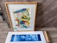 Wide view of both framed abstract colorful painting and unframed blue sky print on floor.