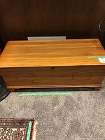 Full front view of the wooden blanket chest showing all sides, wheels at the bottom, and decorative paneling.