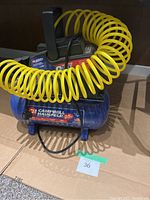 Full view of Campbell Hausfeld air compressor with attached yellow coil hose up front on box.