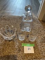 Full set on carpeted floor including square glass decanter with faceted stopper, two etched glasses, and tulip-shaped dish.
