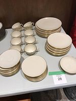 Full view of the dinnerware set showing stacks of plates, cups, and saucers, all white with gold trim.