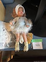 Full view of the Barbara Ann Scott doll lying down, showing her white polka dot dress with fur trim, headscarf, and tan ice skates.