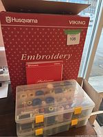 Red Husqvarna Viking outer box labelled 'Embroidery' with small red Platinum manual booklet in front and two clear thread cases below