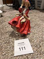 Full view of the Royal Doulton figurine showing the figure of a woman with a flowing red dress and wide-brimmed hat