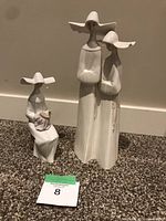 Two Lladro porcelain figurines: one with two standing figures, one seated figure holding object, on carpeted floor with lot card