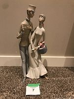 Front view of Lladro couple figurine showing elegant man with a top hat and woman holding a polka-dotted hatbox with flowers.