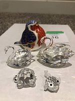 Photo showing all five ornaments together: two clear Swarovski swan crystal figurines, a turtle and fish Swarovski crystal figurine, and a ceramic Royal Crown Derby bird paperweight in blue, orange, and gold.