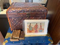 Photo of the rattan box, three small bibles with leather covers, and one print depicting three women in traditional clothing.