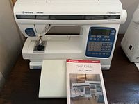 Front view of sewing machine on table with extension table removed and user’s guide placed in front