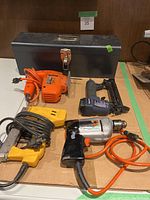 Photo of the toolbox and five tools laid out on cardboard including jig saw, drill, electric and manual staplers.