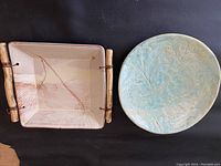Two pottery dishes side by side showcasing the rectangular dish with wooden handles and pine needle imprint alongside the round light blue leaf-impressed plate.