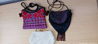 Two small ladies bags on a wooden surface: one bright multicolored hand-stitched bag and one Victorian-style beaded bag with purple and black tones.