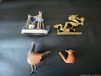 Four items on black background: brass dragon, wooden toy trawler, metal chicken sculpture, and clay bird whistle.
