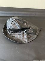 Side view of black shiny oilskin Sou'wester hat showing the wide brim and overall shape.