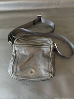 Black leather purse front view showing zippered pocket, round metal accent, and adjustable strap