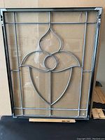 Frontal photo of an antique leaded glass window featuring an acorn-shaped design in metal cames within a rectangular frame.