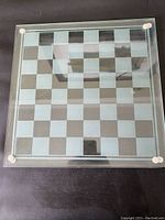 Top view of glass chess/checkers board showing the clear and opaque checkered squares and round rubber feet at corners.