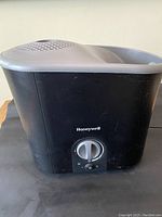 Front and side view of black Honeywell warm mist humidifier with gray top, showing dial control and mist vent.