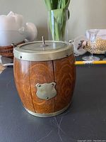 Front view of vintage solid oak barrel-shaped ice bucket with silver plated crest and handle on lid.