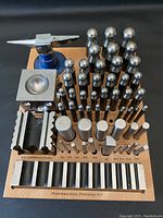 Full kit on wooden stand showing doming punches in three size rows, forming punches, swage slots and anvil at rear