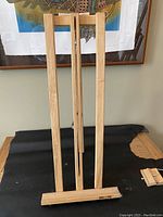 Front view of the easel folded flat, showing slim natural light wood frame and carrying handle at top.