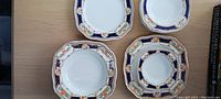 Top view of four small side plates with scalloped edges and decorative cobalt blue border with floral accents and gold trim