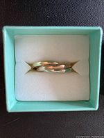 Tri-gold trinity wedding ring resting in foam insert within a light turquoise box