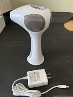 White handheld laser device and charger on black surface